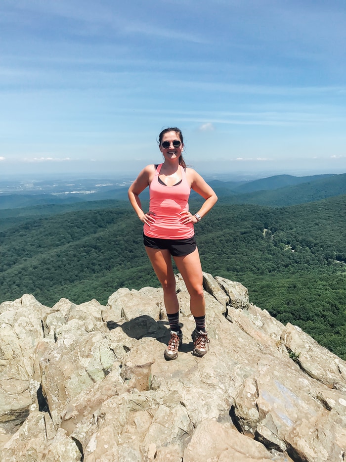 A woman smiling in workout attire at the top of a mountain.