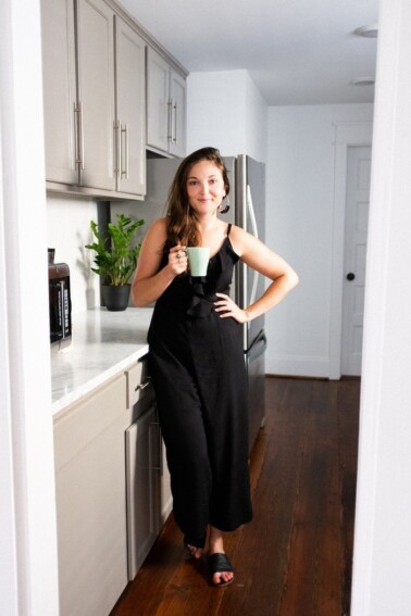 Women in a black jumpsuit in a kitchen with a mint green coffee mug.