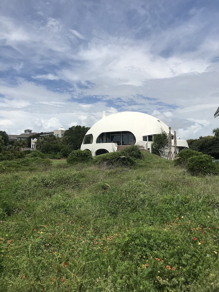 A white dome building surrounded by green plats and a blue sky with many clouds.