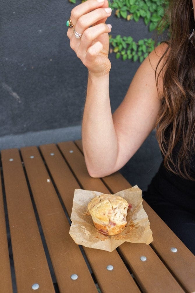Woman resting an elbow on a wooden cafe table. A strawberry muffin is on the table.