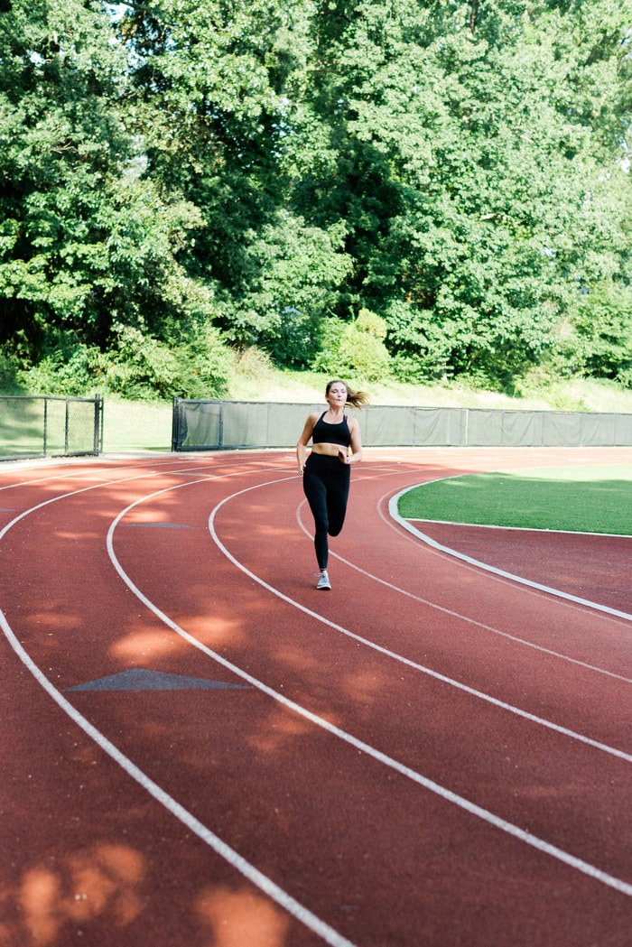 Women running on a track with black running tights and black sports bra.
