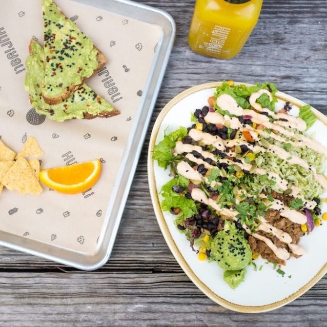 Corn and bean salad, avocado toast on a tray, and a bottle of juice all on a table.