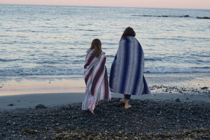 PIN THIS--> A Trip to York, Maine Two women holding patterned blankets around themselves, walking barefoot on a pebble beach in Maine.