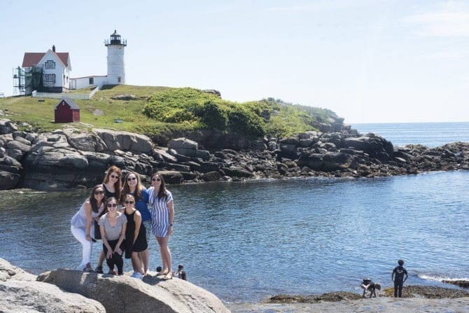 PIN THIS--> A Trip to York, Maine A group of 6 women posing on a rock in front of Nubble Lighthouse in Maine. The coast is rocky and filled with grass. The lighthouse and house next to it look over the sea.