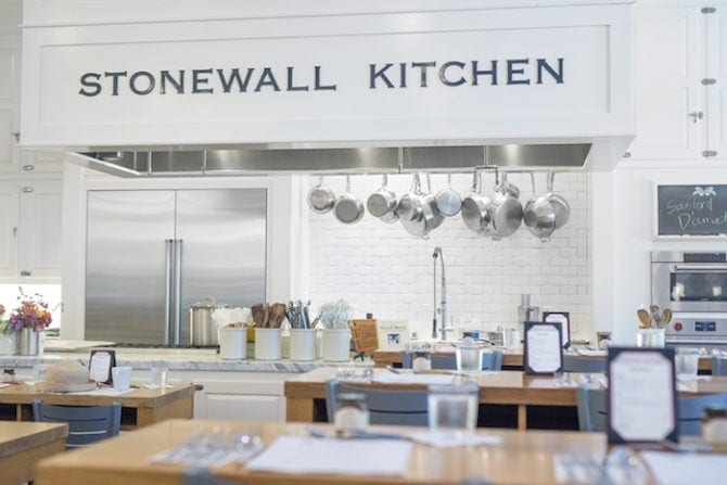 PIN THIS--> A Trip to York, Maine Photo of Stonewall Kitchen-- wooden cooking tables in front of an open kitchen with pots hanging from the ceiling.