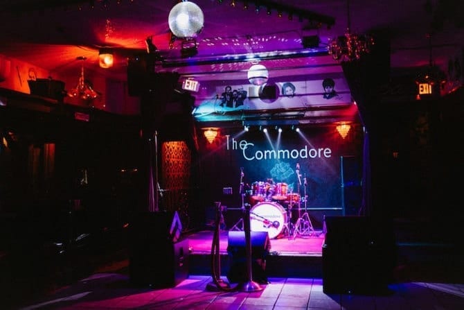 The Commodore, a night spot with a band stage and purple and red lighting.