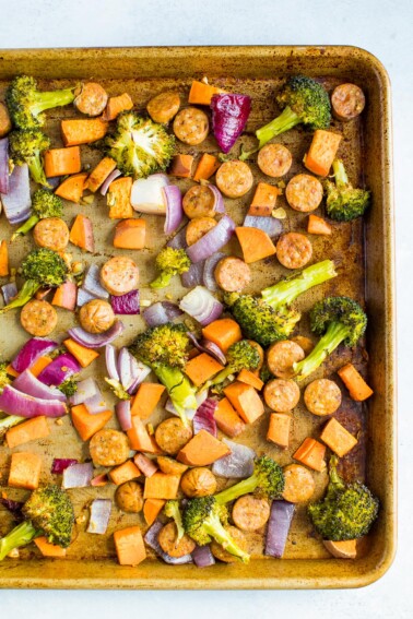 Sausage, broccoli, butternut squash and onion on a baking tray.