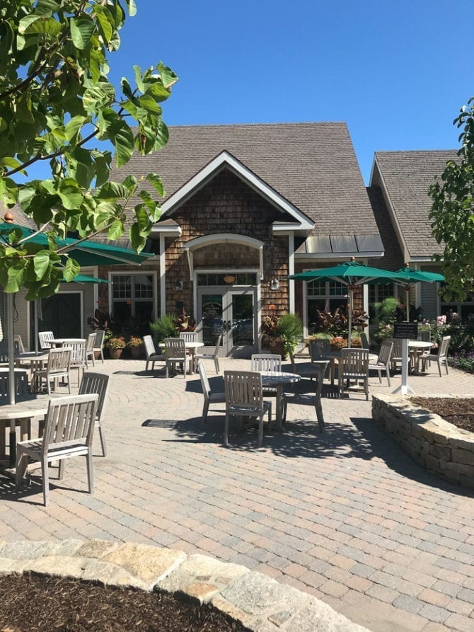 PIN THIS--> A Trip To York, Maine View of an open patio with tables and chairs, and a wood shingle home in the background. There are umbrellas and trees.