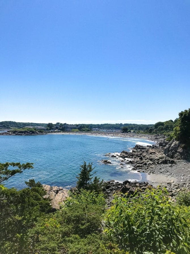 PIN THIS--> A Trip to York, Maine A view from Cliff Walk in York, Maine. Green tress and bushes are next to a rocky beach and blue ocean water.