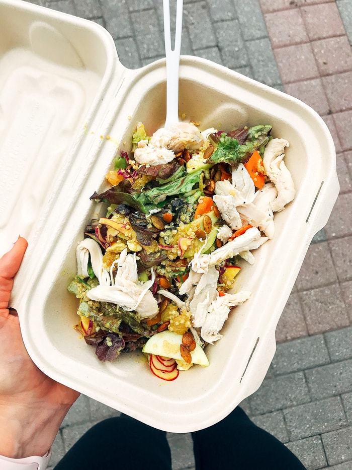 Woman holding a to-go container with a kale chicken Caesar salad.