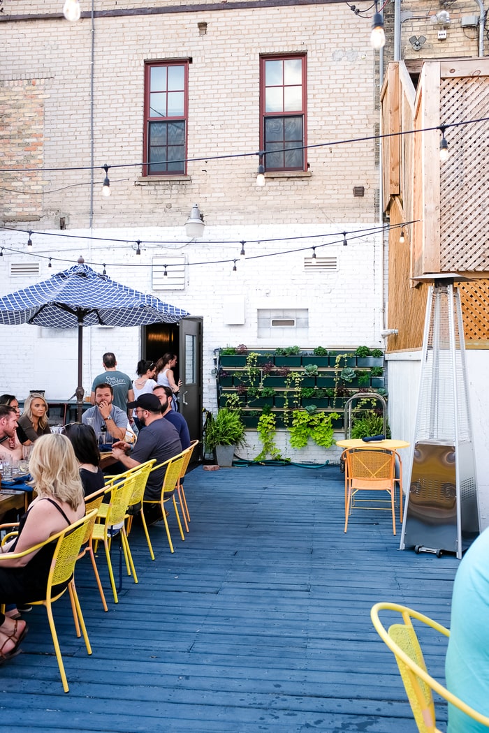 Outdoor patio by a painted brick buildings. Umbrellas and outdoor tables are on the patio of this bar.