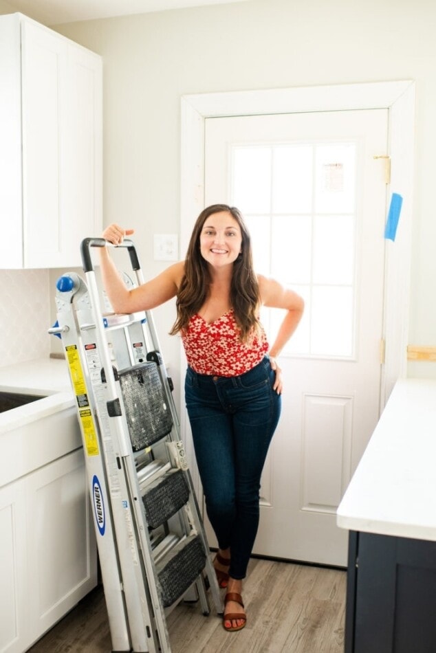 Woman standing in a partially renovated kitchen, leaning on a ladder.