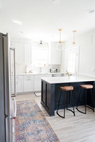 White kitchen with navy blue island and wood and metal modern stools.