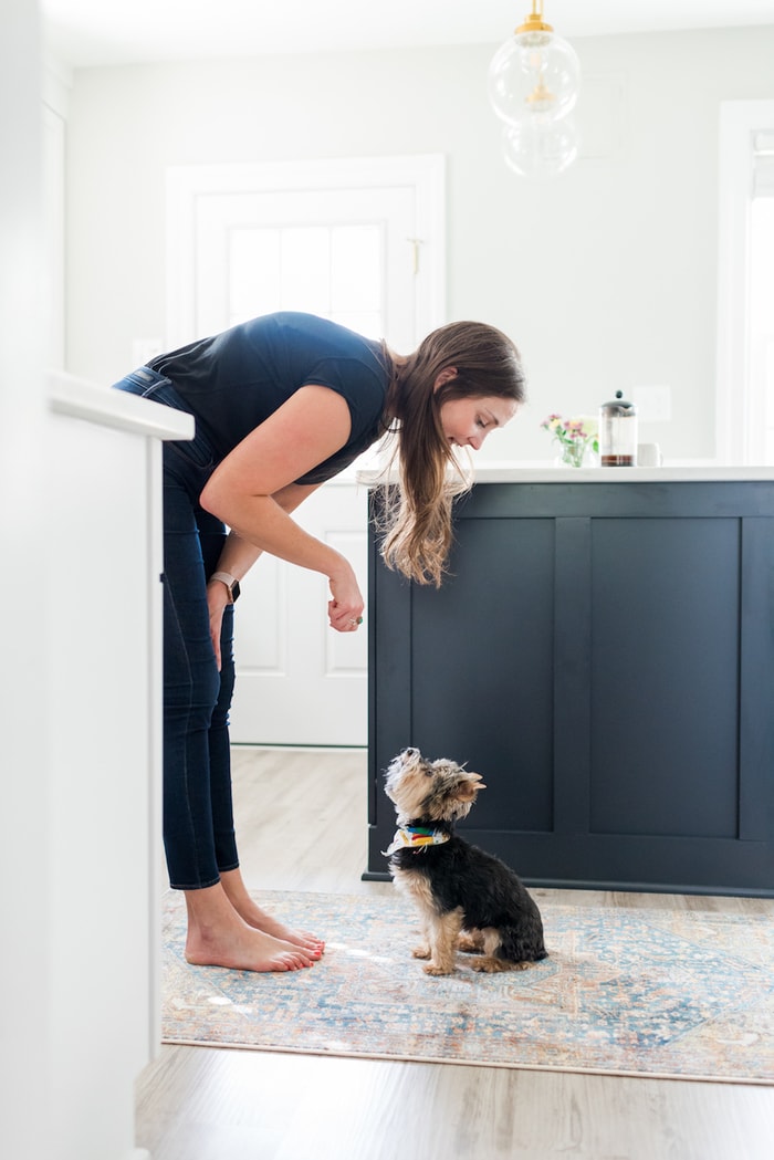Woman engaging with dog in a white kitchen with black island.