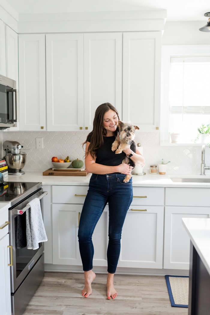 Woman smiling, holding a dog, in a white kitchen.