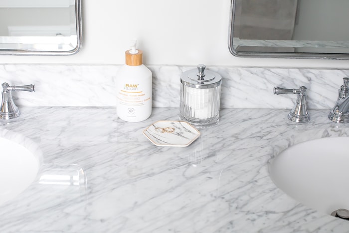 Renovated bright small bathroom with marble floors and white vanity with marble countertop.