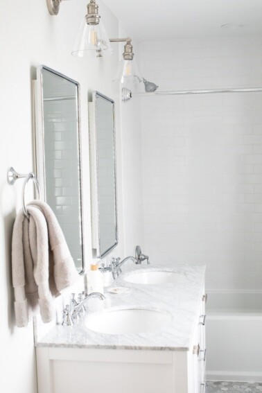 Renovated bright small bathroom with marble floors and white vanity with marble countertop.