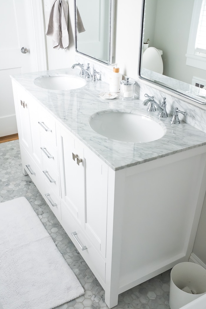 Renovated bright small bathroom with marble floors and white vanity with marble countertop.