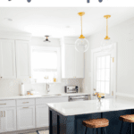 White kitchen with navy island, marble countertops, and wooden stools.