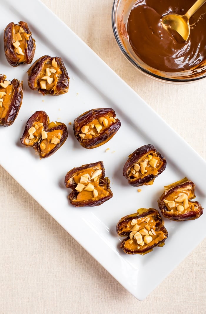 Medjool dates, pitted and split open with peanut butter and peanuts stuffed inside. Melted chocolate with a gold spoon on the side. 