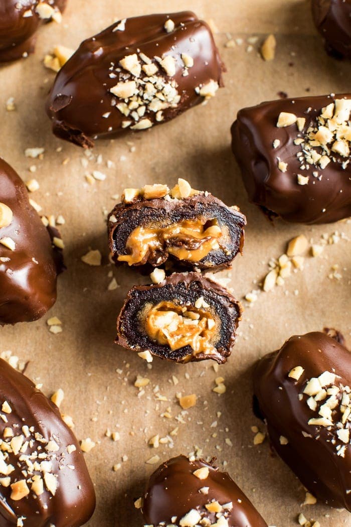 Chocolate covered peanut butter stuffed Medjool date cut in half, resting on top of another stuffed date. There are more snickers stuffed dates in the background.