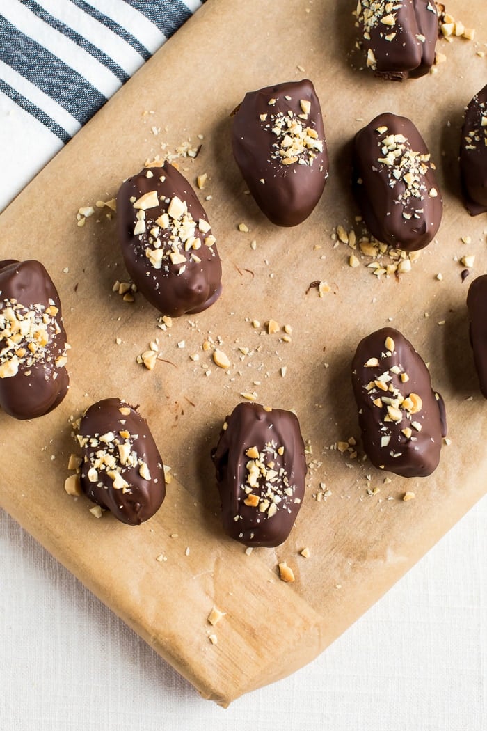 Chocolate covered medjool dates with crushed peanuts on top, scattered over a parchment lined cutting board.