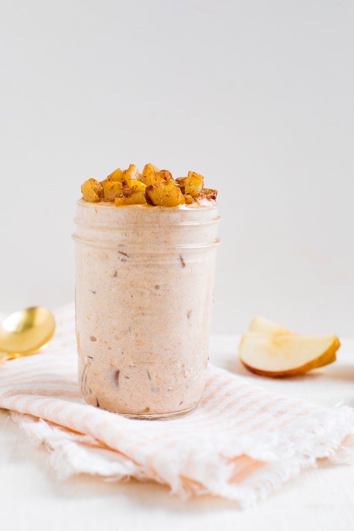 Glass jar filled with apple pie overnight oats and topped with cinnamon apples. Apple slices and a spoon.