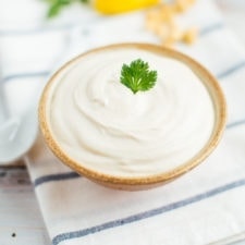 Blended cashew sour cream in a tan bowl with a sprig of parsley in the middle.