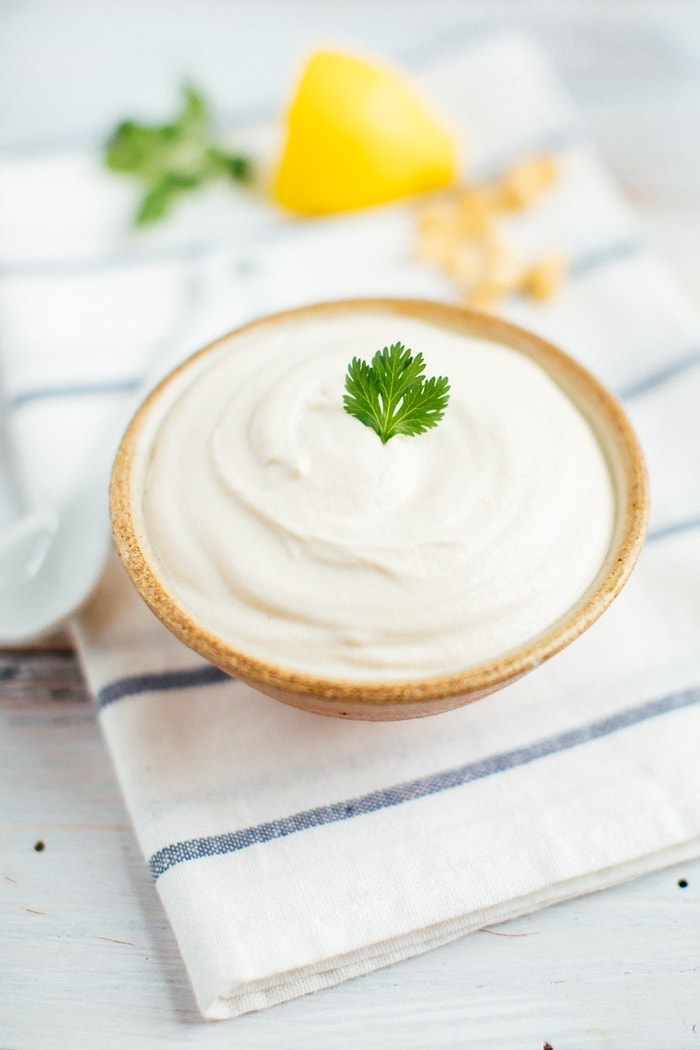 Blended cashew sour cream in a tan bowl with a sprig of parsley in the middle. 