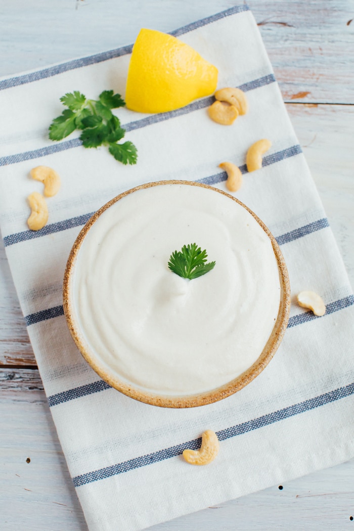 Blended cashew sour cream in a tan bowl with a sprig of parsley in the middle. 