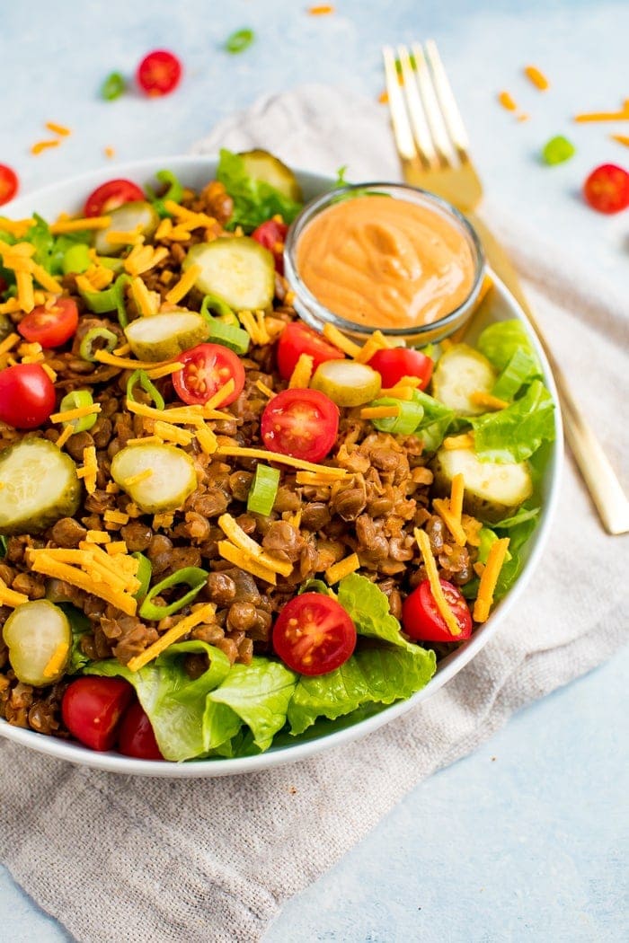 Vegan cheeseburger salad-- romaine lettuce topped with lentil walnut "meat", vegan cheese, tomatoes, pickles, onions, and a cashew cream special sauce. A folk is on the side of the plate.