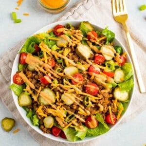 Vegan cheeseburger salad, dressing drizzled on top, on a plate with fork and neutral napkin.