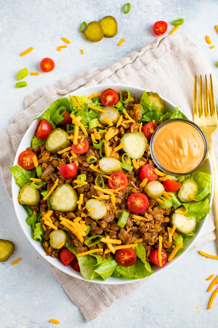 Vegan cheeseburger salad-- romaine lettuce topped with lentil walnut "meat", vegan cheese, tomatoes, pickles, onions, and a cashew cream special sauce. A folk is on the side of the plate.