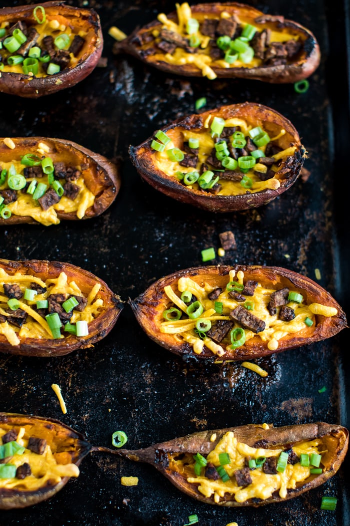 Baked sweet potato skins on a baking stone. The cheese and bacon is melted and crispy. Chives are sprinkled on top.