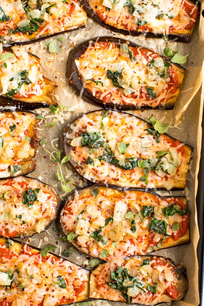 Slices of eggplant on a baking sheet with parchment paper-- they are eggplant pizzas topped with cheese, sauce, and some greens.