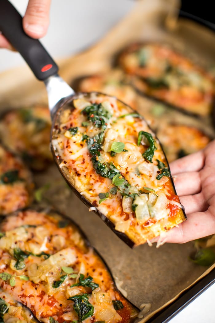 Spatula and hand picking up a slice of eggplant pizza.