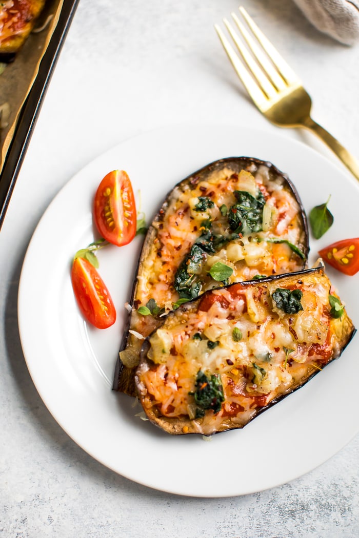 Two piece of eggplant pizza on a plate with a couple slices cherry tomatoes next to them, and a fork to the side.