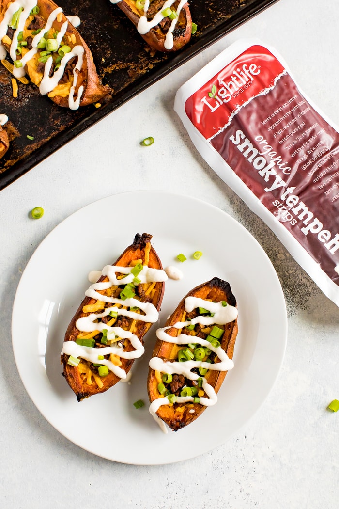 A plate with two sweet potato skins, and a package of tempeh bacon, and the baking stone with the sweet potato skins next to the plate.