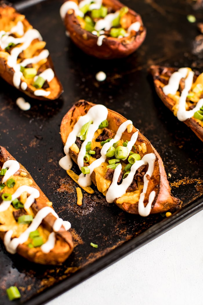 Close up shot of a sweet potato skin on a baking stone. The skins are filled with vegan cheese, bacon, chives, and sour cream drizzle.