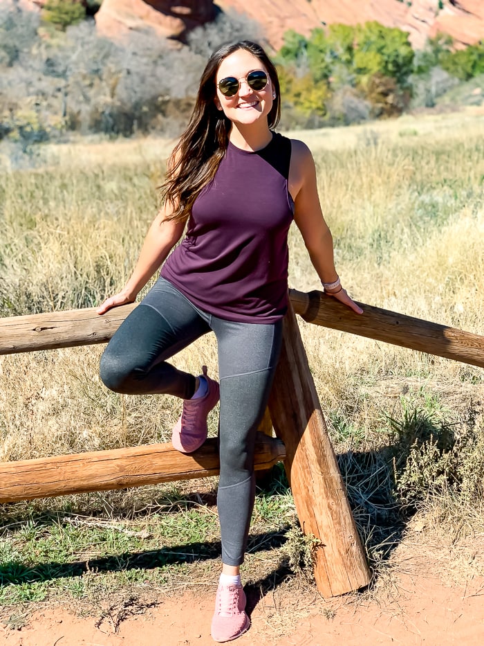 Woman in workout gear standing in front of a fence at Red Rocks on a hiking trail.