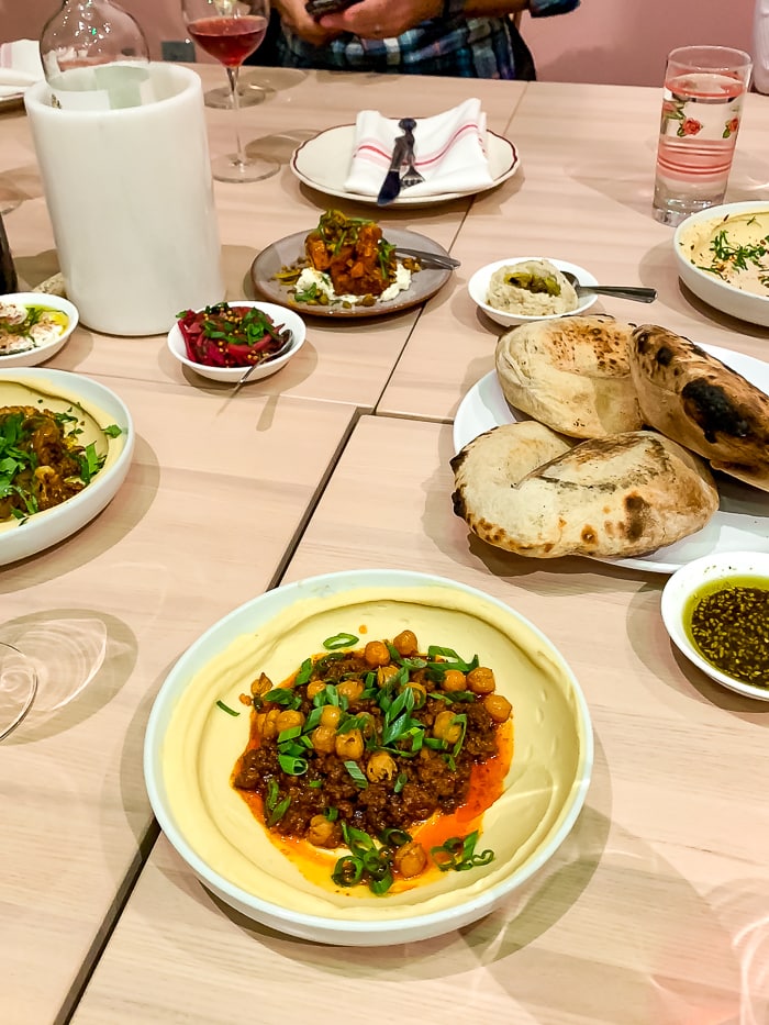 Spread of food at an Israeli restaurant in Denver with plates of chickpea hummus, bread, and drinks.