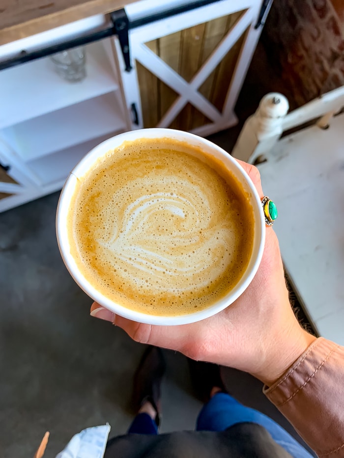 Woman holding a latte from Black Eye Coffee in Denver. She has a stone ring on her finger.