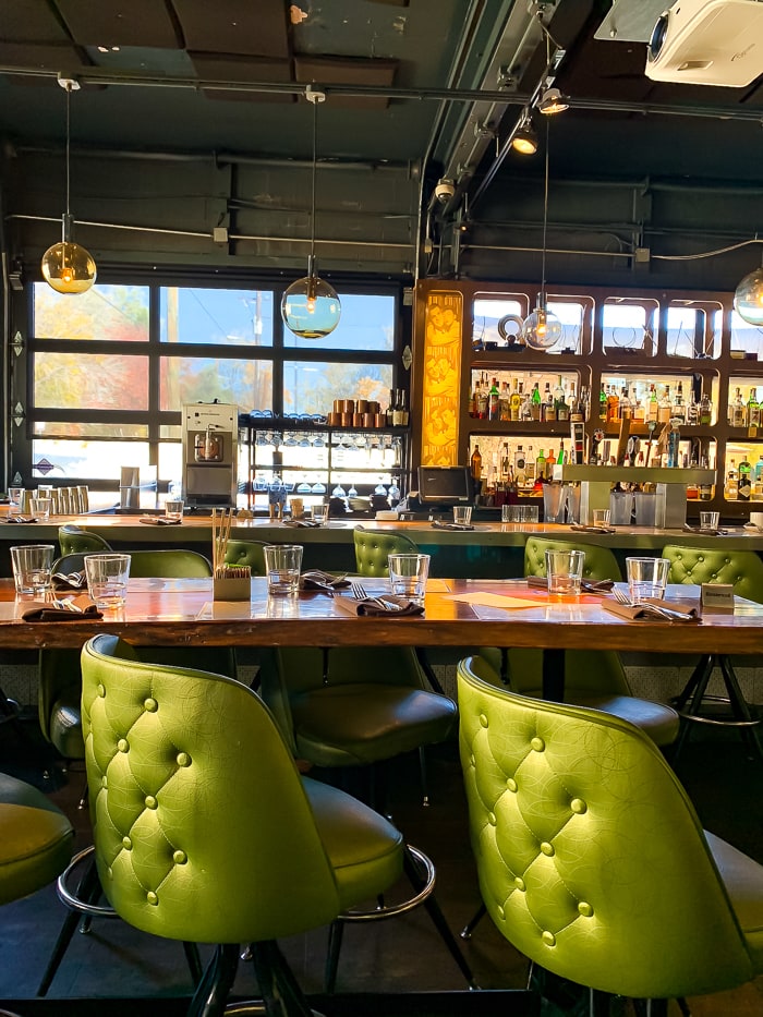 Chairs at a long community table. Two bar tables next to each other and globe lights hanging from an industrial ceiling.