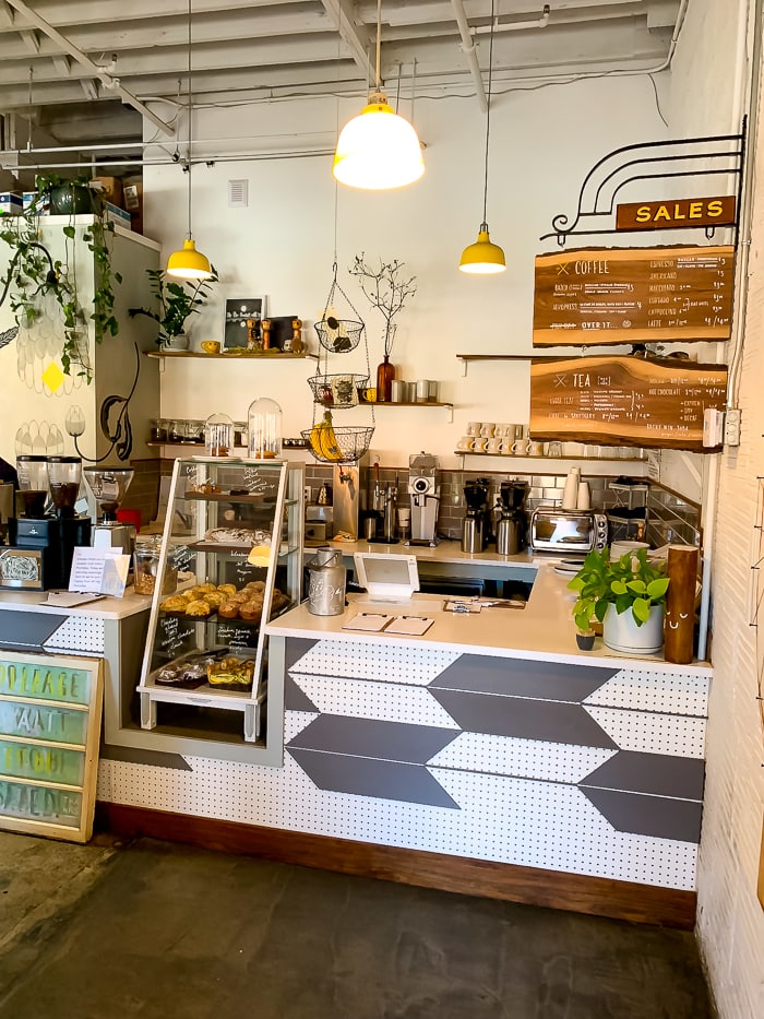 Counter at a coffee shop in Denver with a pastry case, hanging lights, and a wooden menu.