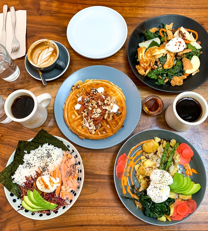 Food spread of breakfast dishes at a restaurant in Denver. Coffee, waffles and some variations of breakfast bowls.