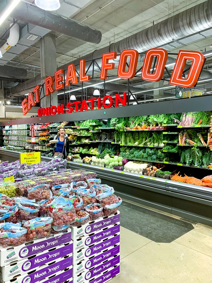 Woman in front of the produce case of Denver's Union Station's Whole Foods. The sign above says "Eat Real Food, Union Station".