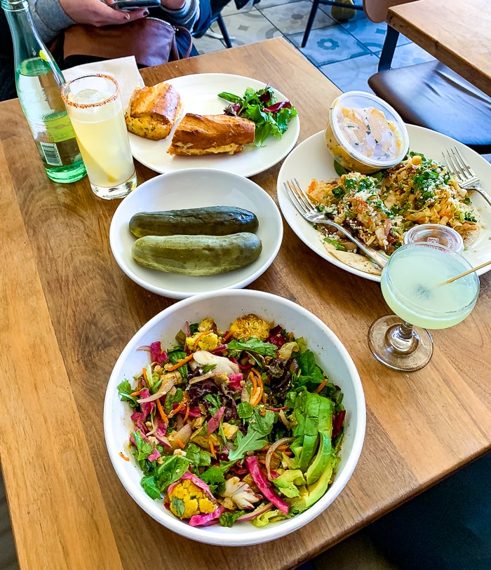 Lunch food table with pickles, sandwiches, and salads. An assortments of cocktails is also on the table.