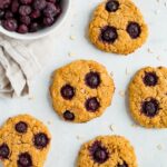 Oatmeal blueberry cookies on a counter next to a bowl of frozen blueberries.