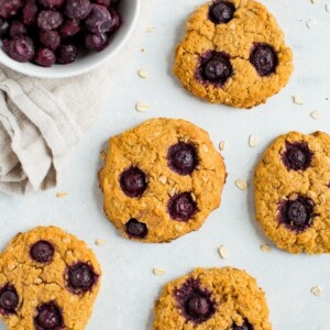 Oatmeal blueberry cookies on a counter next to a bowl of frozen blueberries.