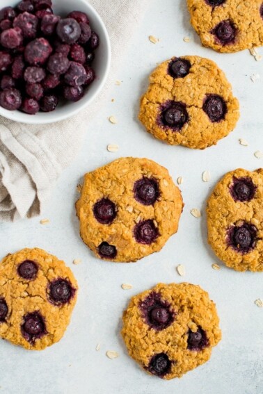 Oatmeal blueberry cookies on a counter next to a bowl of frozen blueberries.